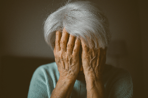 elderly woman covering her face; looking upset