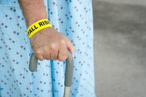 close-up side view of elderly man's hand holding a cane wearing hospital robe